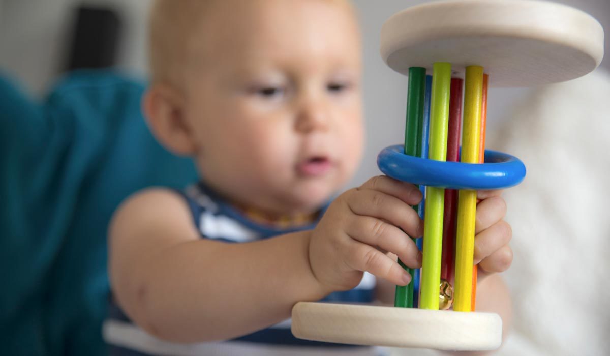Moet-een-kind-leren-hoe-het-moet-spelen Een baby in een gestreept shirt is geconcentreerd en leert spelenderwijs, terwijl hij bezig is met een kleurrijk houten speeltje versierd met ringen.