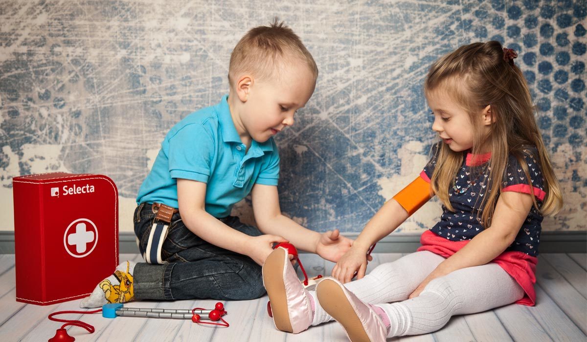 Twee kinderen spelen tijdens het rollenspel spelen met peuters doktertje met een speelgoed doktersdoos; de jongen controleert zorgvuldig de arm en het been van het meisje.