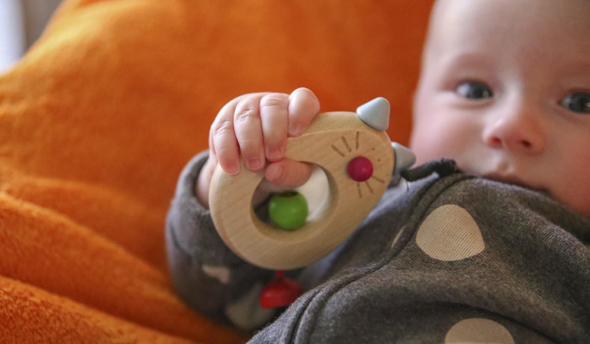 Een baby die zijn zintuigen gebruikt, houdt een houten speeltje vast terwijl hij comfortabel op een oranje deken ligt.