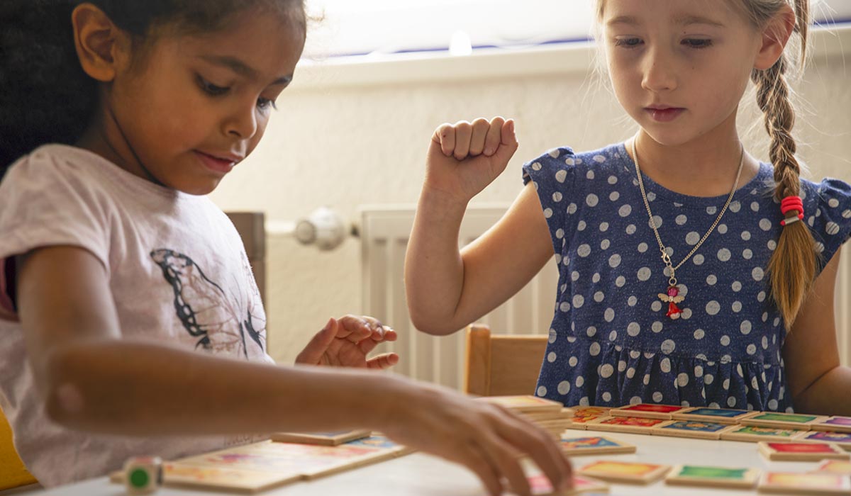 hout-speeltjes-sekbeddendief Twee jonge meisjes lachen samen en bouwen vriendschap op terwijl ze samen aan een gezellige tafel binnenshuis een bordspel spelen.