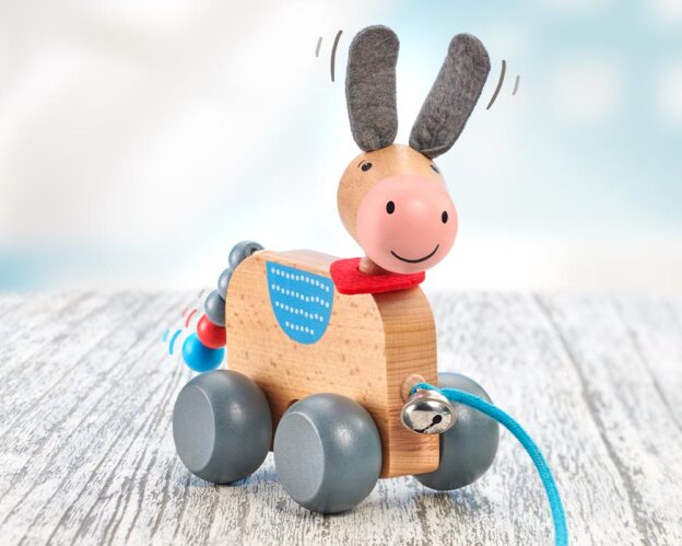 Massief houten trekezel op wielen, versierd met een rode kraag en blauw touw, staat trots op een gestructureerd oppervlak.